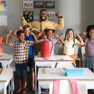 Multiracial elementary students and african american young male teacher flexing muscles. unaltered, education, firefighter, safety, protection, teaching and school concept.